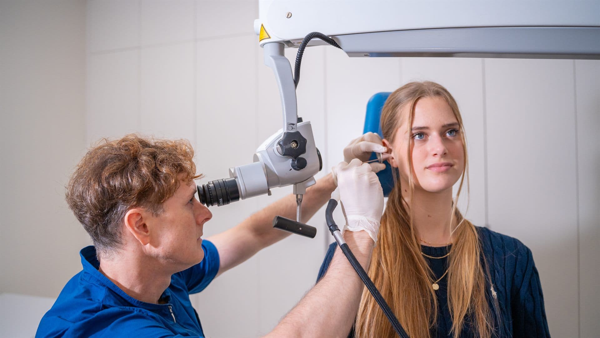 ORL specialist z otomikroskopom pregleduje zamašeno uho pacientke v ambulanti GM-O v Ljubljani